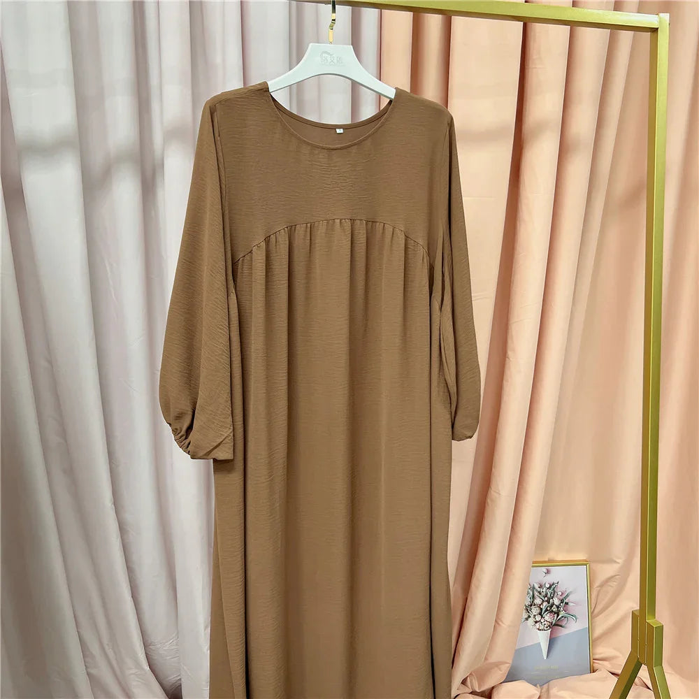 Brown long sleeve maxi dress hanging on white hanger against beige and pink fabric backdrop