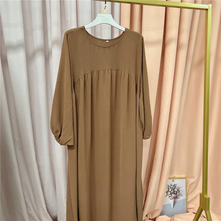 Brown long sleeve maxi dress hanging on white hanger against beige and pink fabric backdrop
