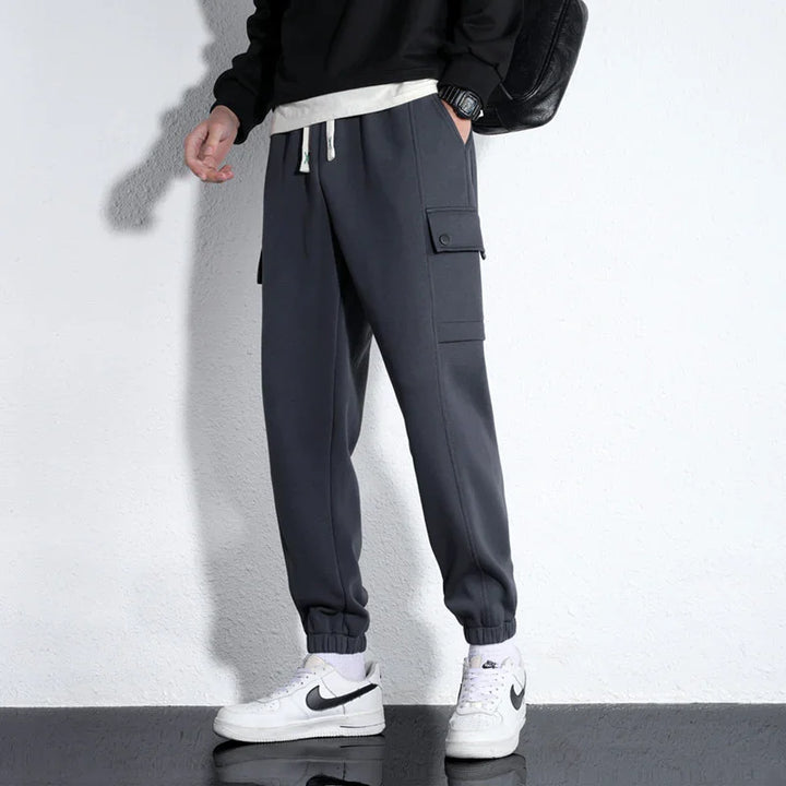 Person wearing dark gray cargo jogger pants with elastic cuffs and white Nike sneakers against white wall