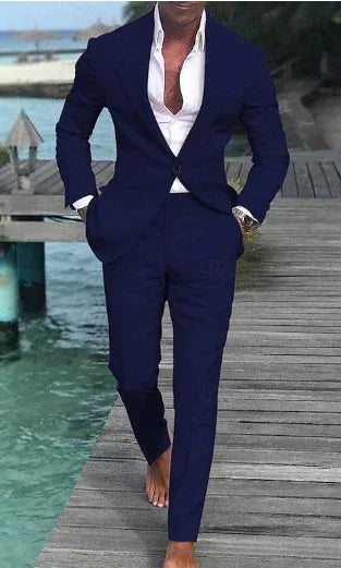 Man wearing a navy blue suit and white shirt walking barefoot on a wooden dock by turquoise water