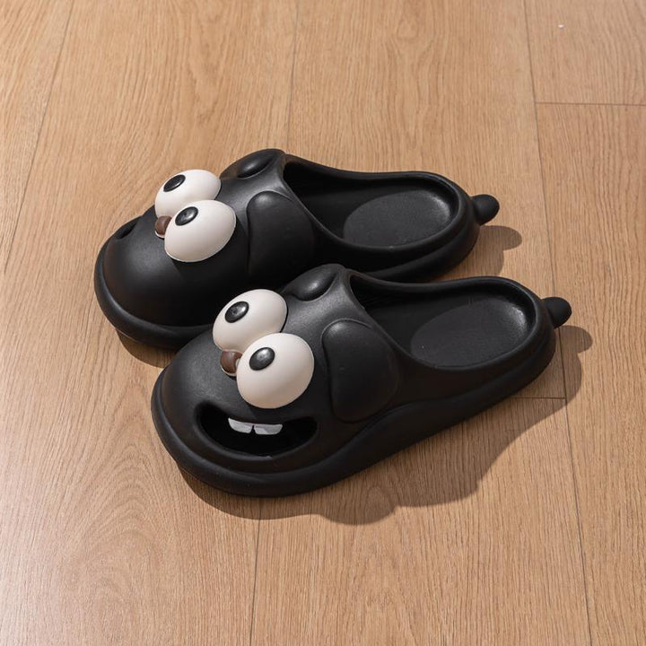 Black cartoon character slippers with large googly eyes and teeth on wooden floor