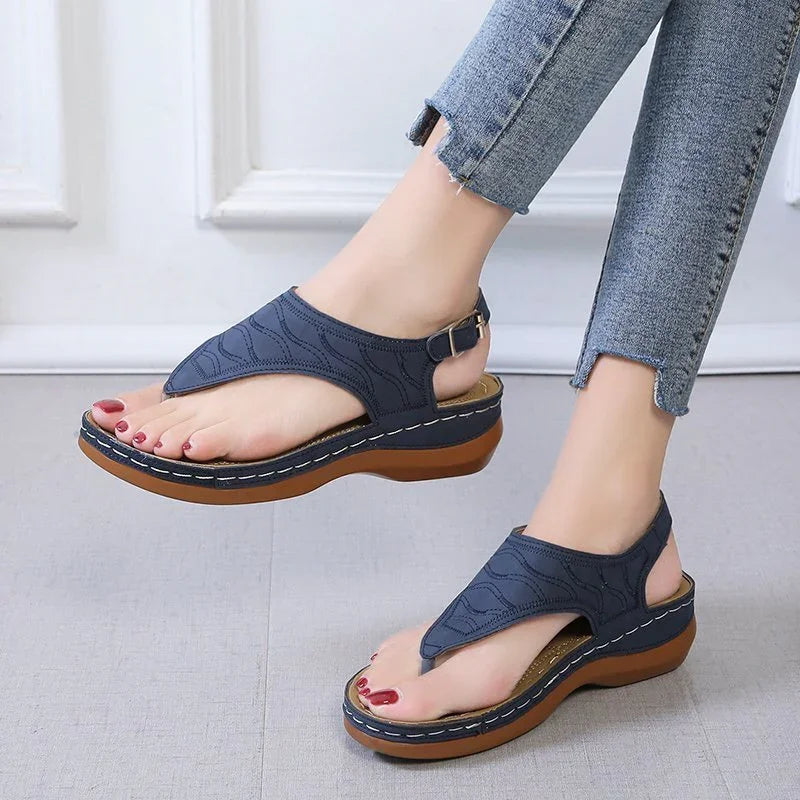 Female feet wearing navy blue wedge sandals with buckle straps and textured sole, paired with cropped jeans
