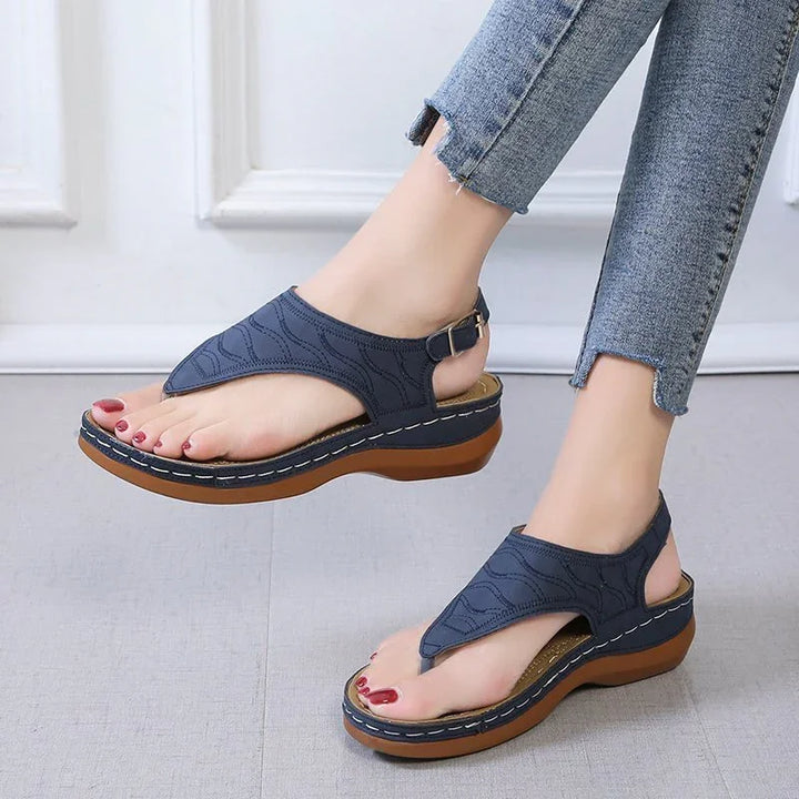 Female feet wearing navy blue wedge sandals with buckle straps and textured sole, paired with cropped jeans