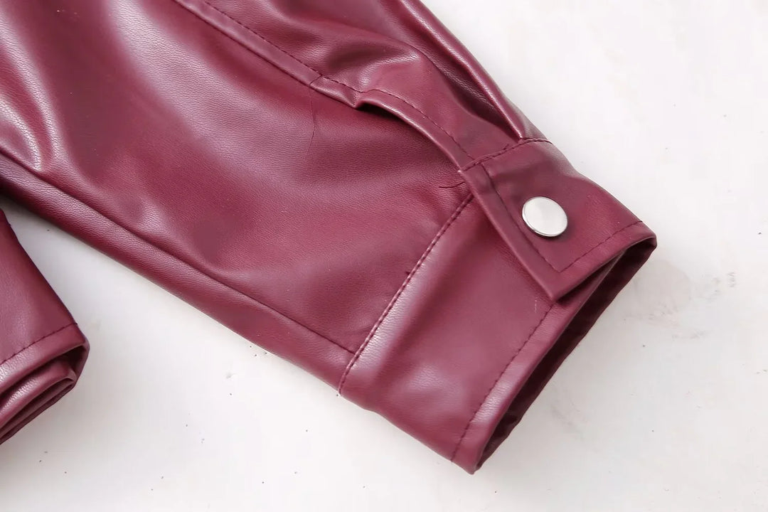 Close-up of maroon faux leather jacket sleeve with silver snap button on white background