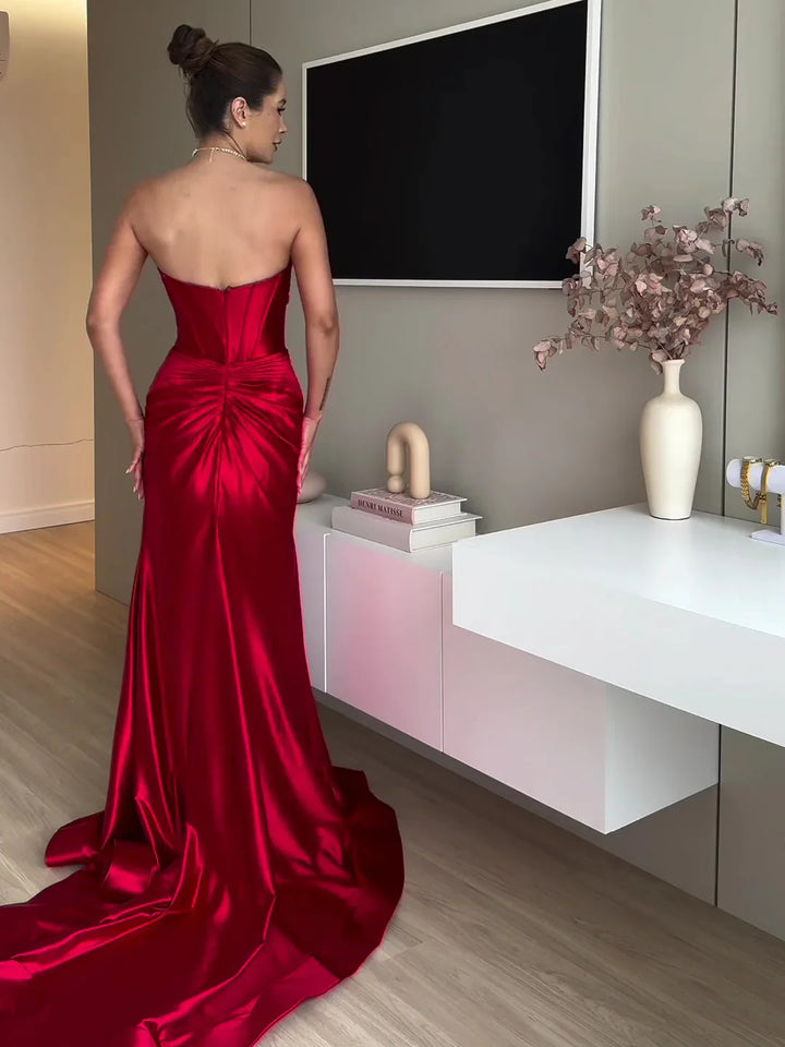 Woman in elegant red satin strapless gown with train standing in a modern room with white furniture