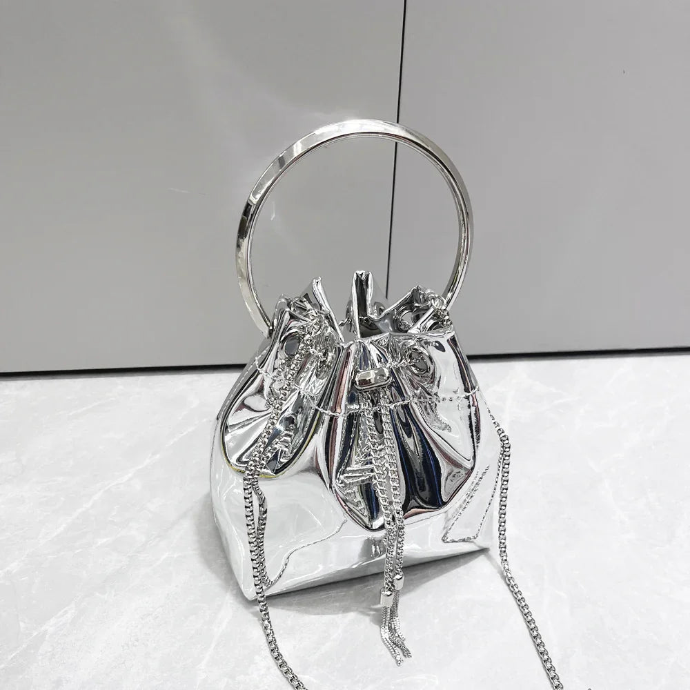 Shiny silver metallic bucket bag with circular handle and chain drawstring on marble surface