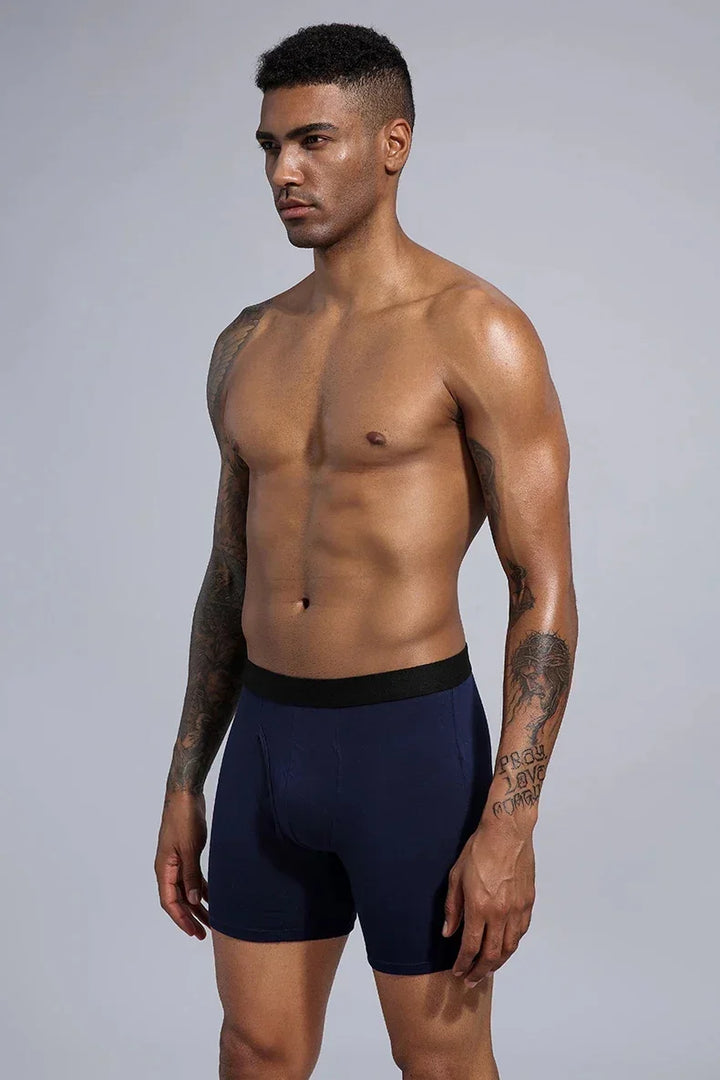 Fit man with tattoos wearing navy blue boxer briefs with black waistband on gray background