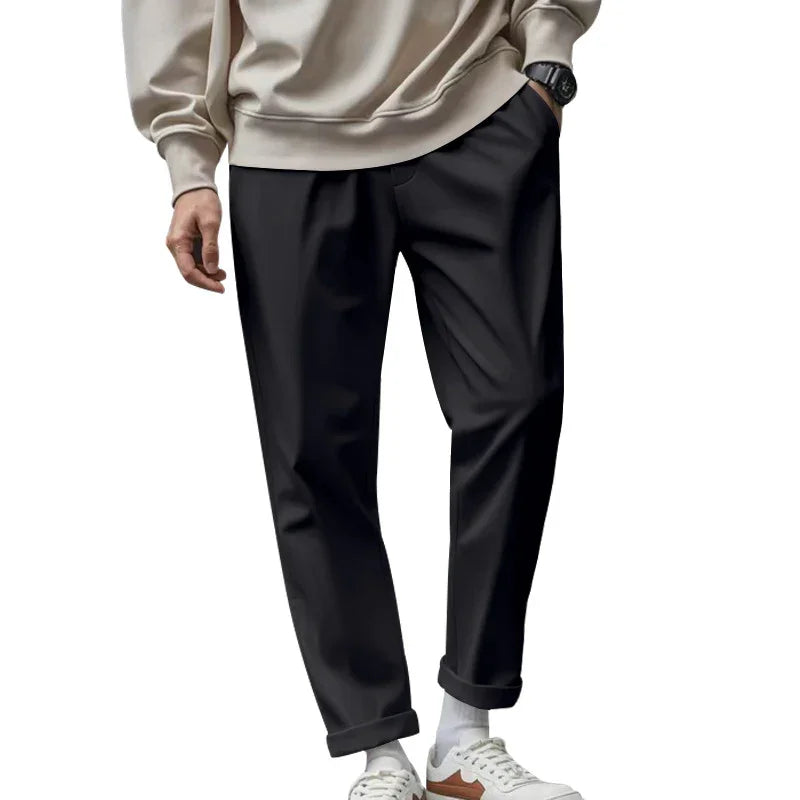 Man wearing black tapered pants, beige sweatshirt, white socks, and white sneakers