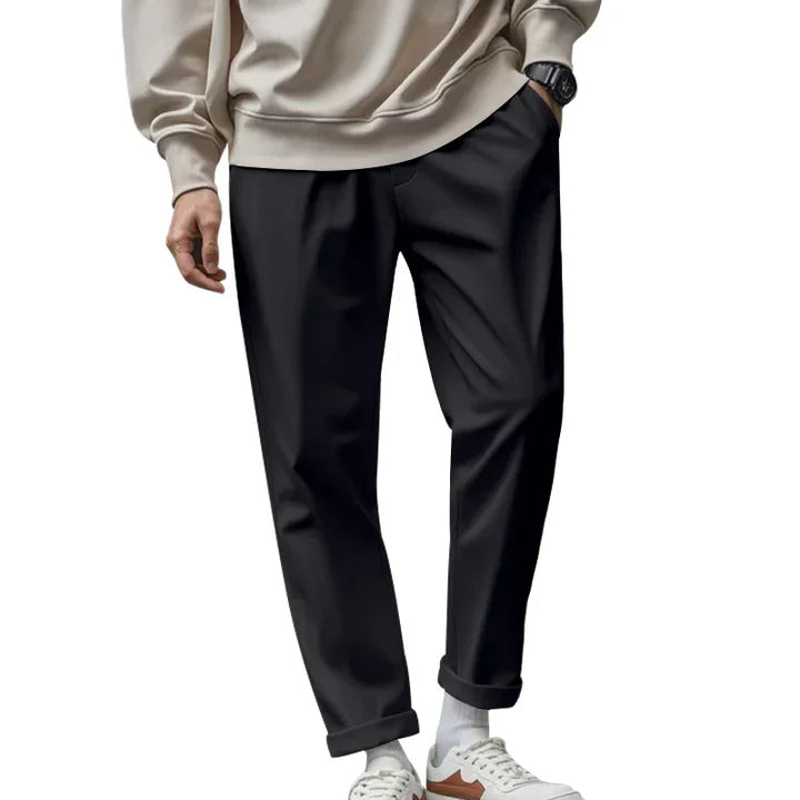 Man wearing black tapered pants, beige sweatshirt, white socks, and white sneakers