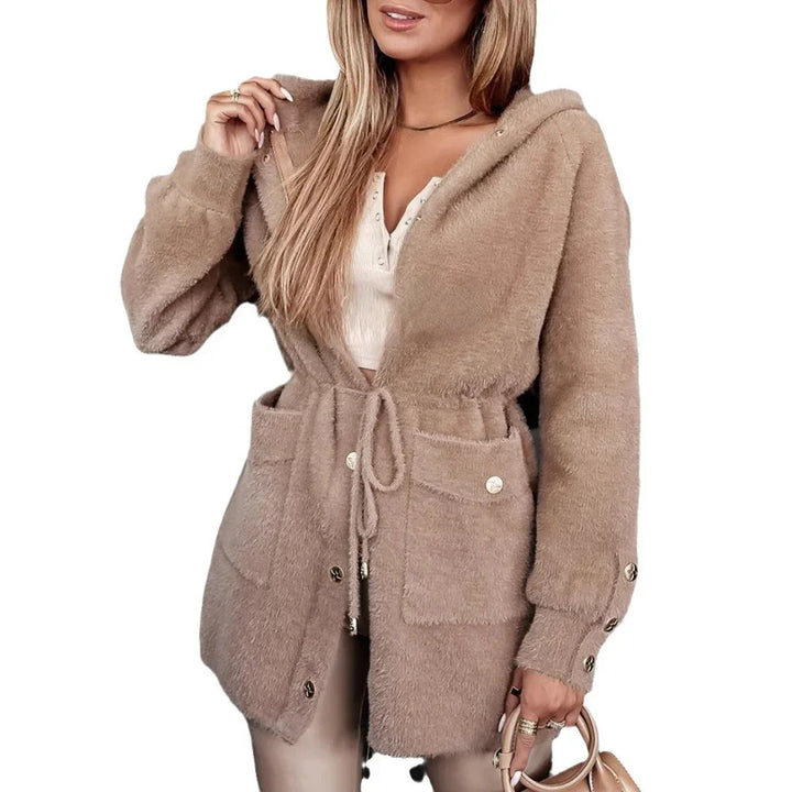 Woman wearing beige fuzzy hooded cardigan with drawstring waist and front pockets, holding a tan handbag