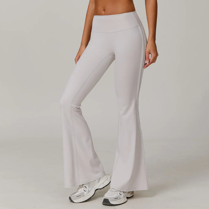 Woman wearing light gray high-waisted flare leggings and white sneakers on neutral background