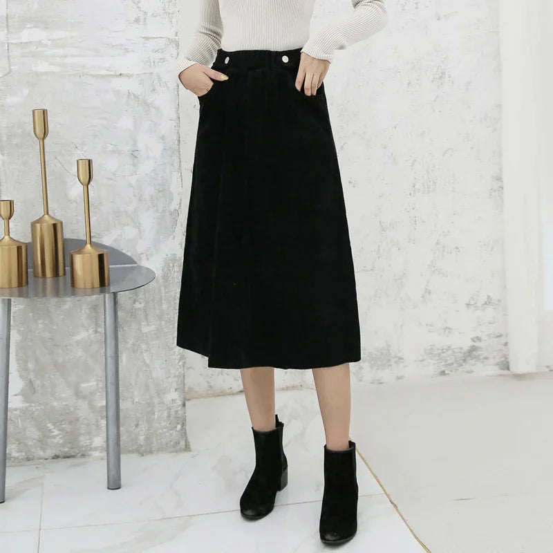 Woman wearing a black midi skirt with pockets and black ankle boots against a textured white wall