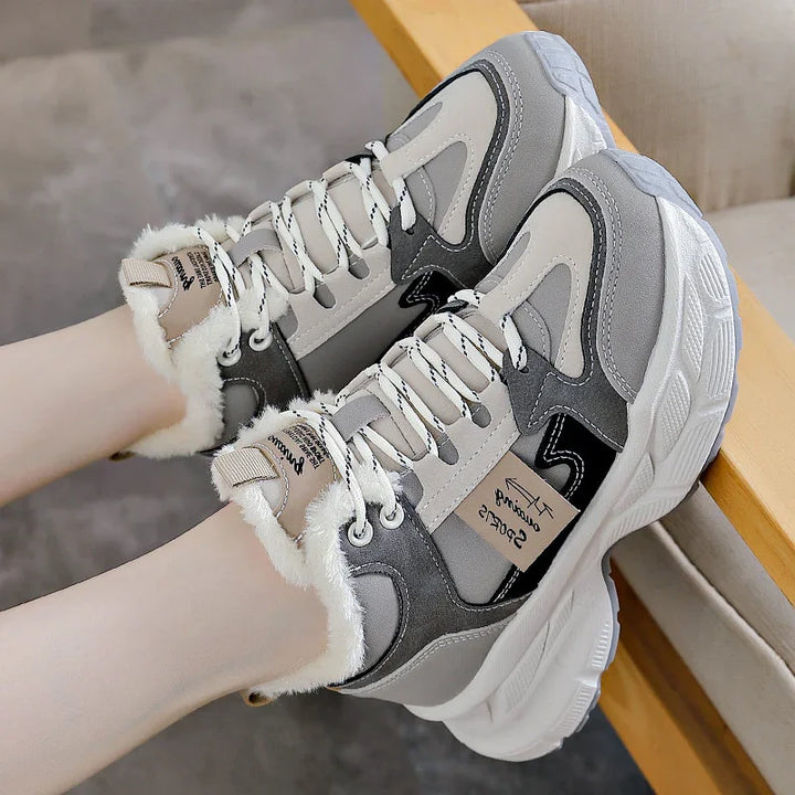 Gray and white casual sneakers with fluffy lining and thick soles worn on feet on a beige chair