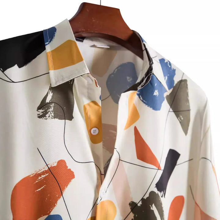 Close-up of abstract printed button-up shirt with blue, orange, yellow, and black shapes on white fabric