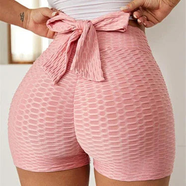 Woman wearing high waisted textured pink shorts with bow tie waist in bright room