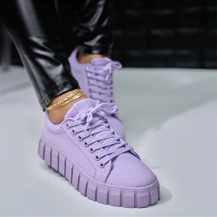 Close-up of lilac platform sneakers with chunky sole worn with black leather pants and gold anklets