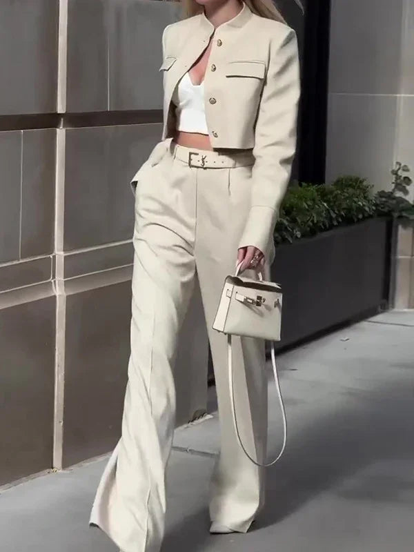 Woman wearing beige cropped blazer and high-waist wide-leg trousers, carrying small structured handbag