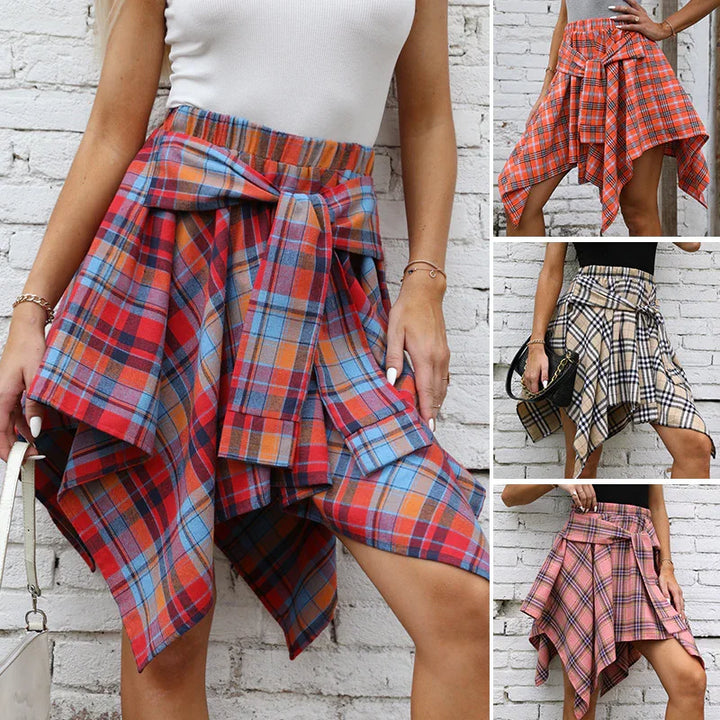 Women wearing asymmetrical handkerchief plaid skirts in red, orange, beige, and pink, styled with tops and accessories against a white brick wall
