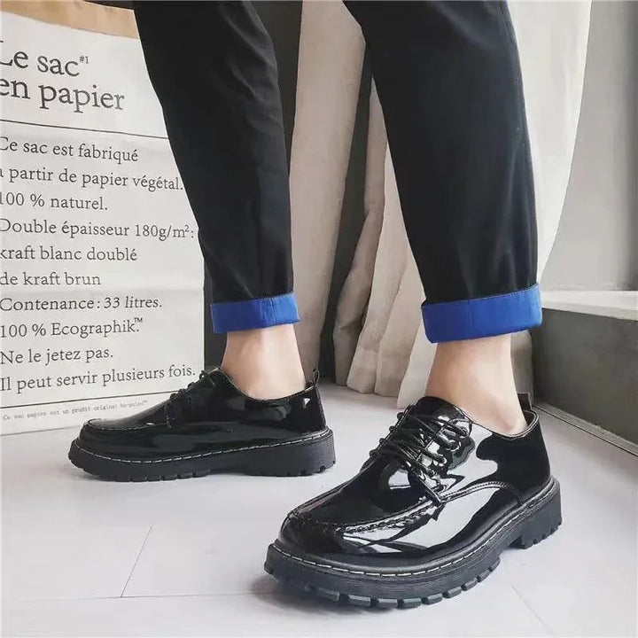 shiny black leather lace-up shoes worn with black pants rolled at the ankle indoors