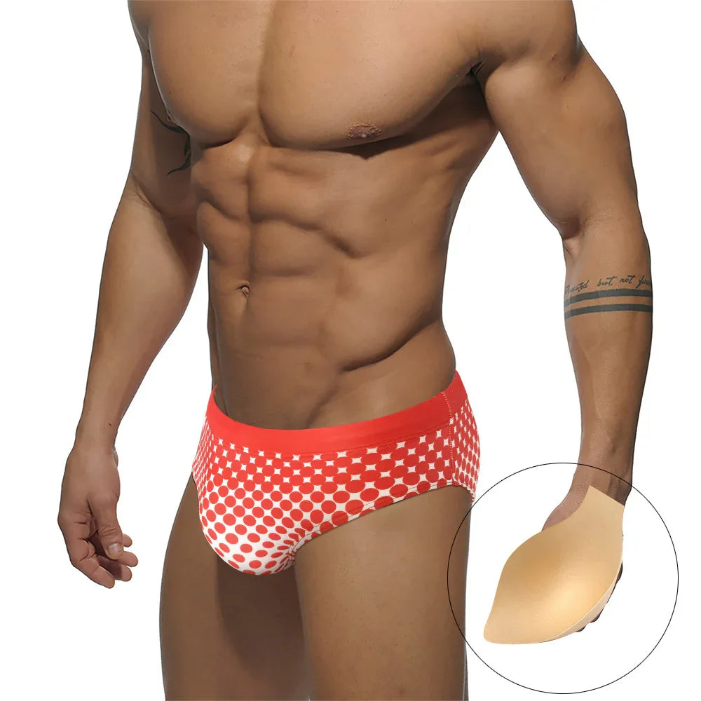 Muscular man wearing red and white polka dot swim briefs, showing silicone butt lifter padding