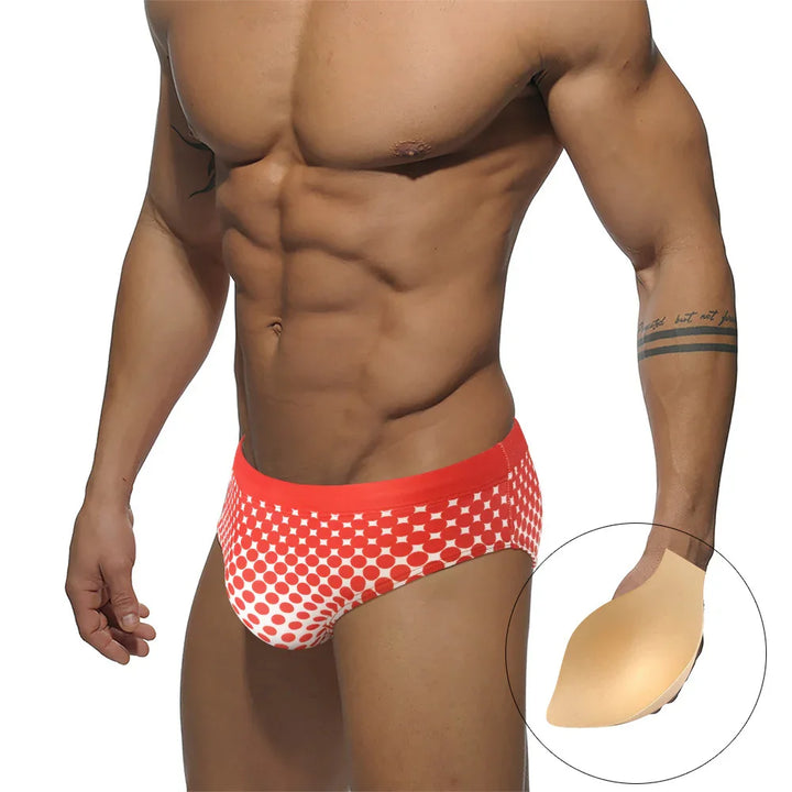 Muscular man wearing red and white polka dot swim briefs, showing silicone butt lifter padding