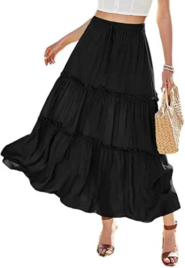 Woman wearing a flowing black tiered maxi skirt with a white crop top and holding a woven handbag