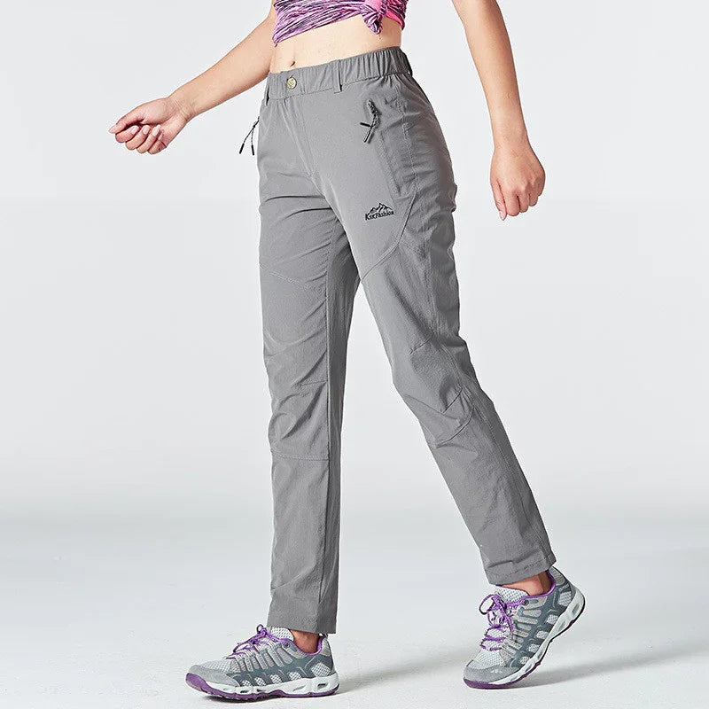 Woman wearing gray outdoor hiking pants and gray purple sneakers on a white background