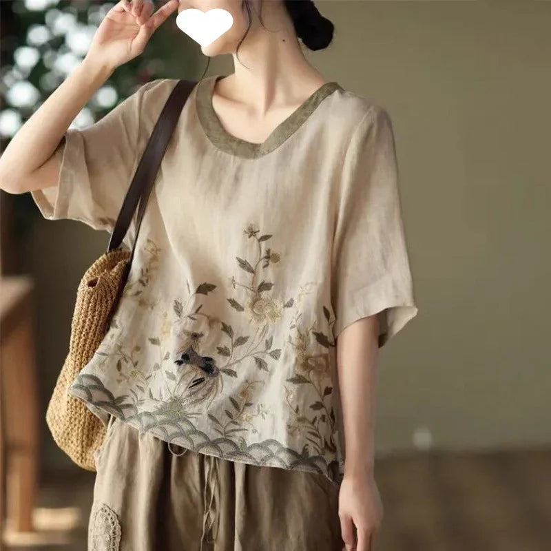 Woman wearing beige embroidered floral linen blouse with brown neckline and carrying woven bag