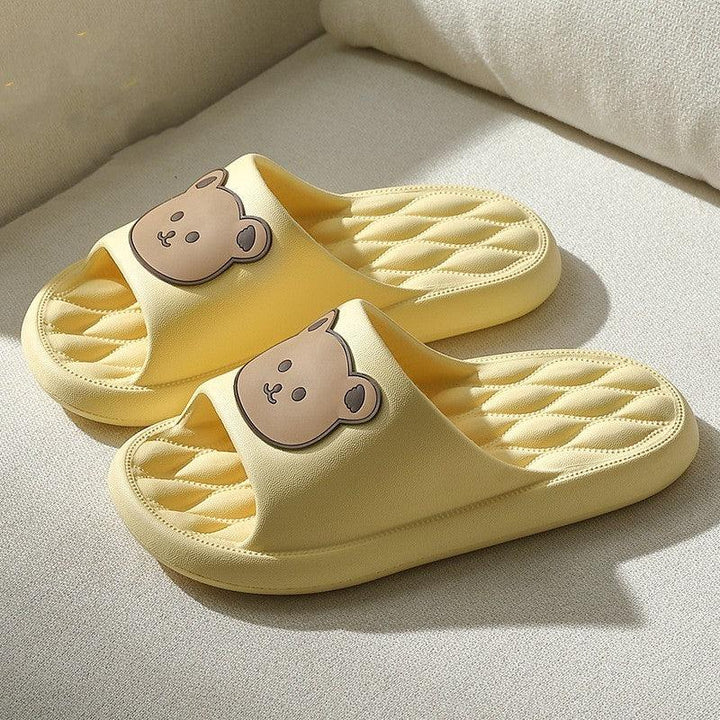 Yellow indoor slippers with quilted soles and cute brown bear faces on straps on beige surface