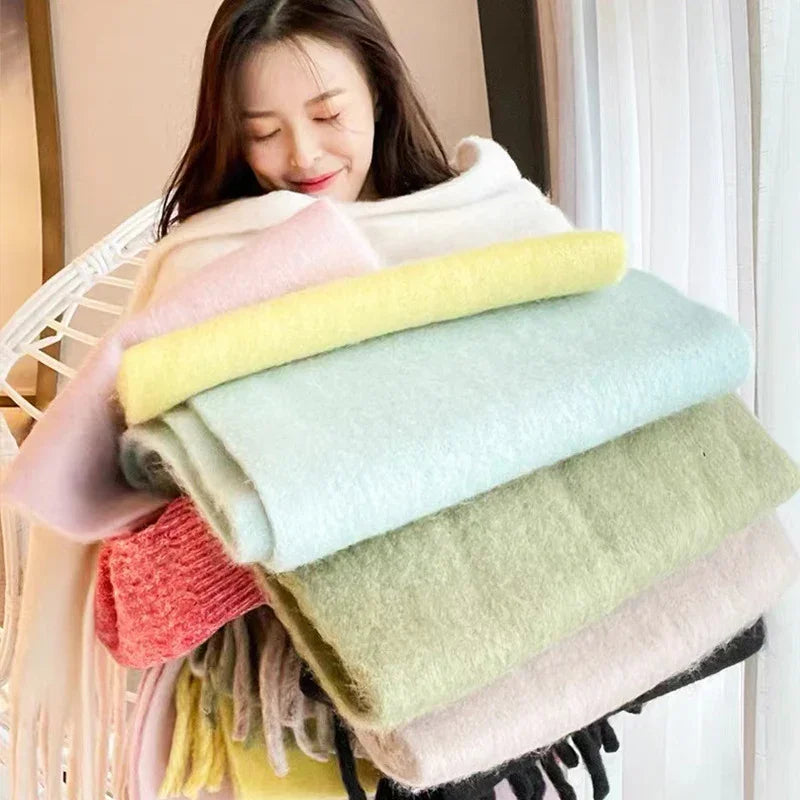 Woman holding a stack of soft pastel-colored woolen scarves in a bright indoor setting