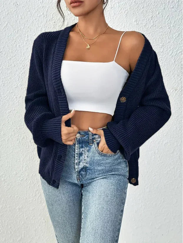 Woman wearing navy blue chunky knit cardigan over white crop top paired with high-waisted light blue jeans