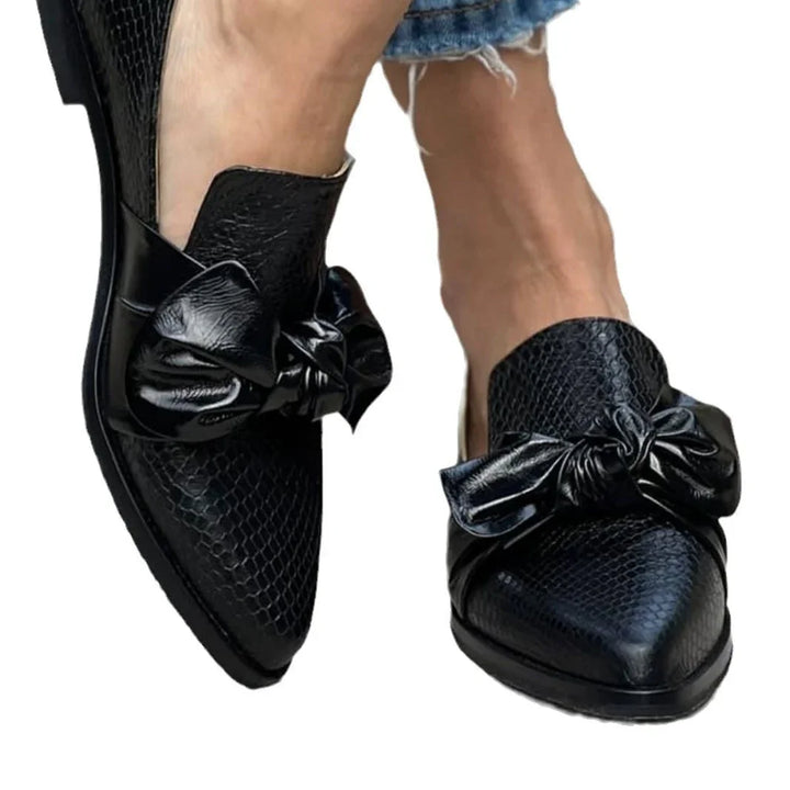 Black textured pointed toe slip-on shoes with large leather bows worn with frayed hem jeans