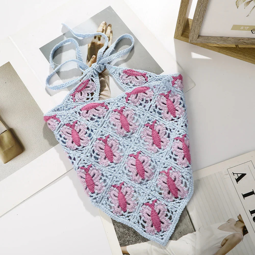 Blue and pink crocheted halter top with floral pattern lying on magazines on white table