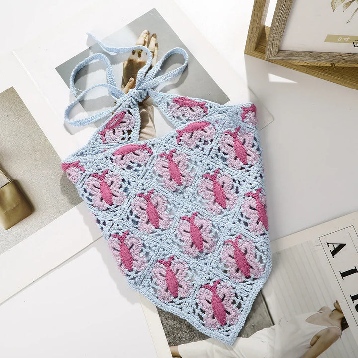 Blue and pink crocheted halter top with floral pattern lying on magazines on white table