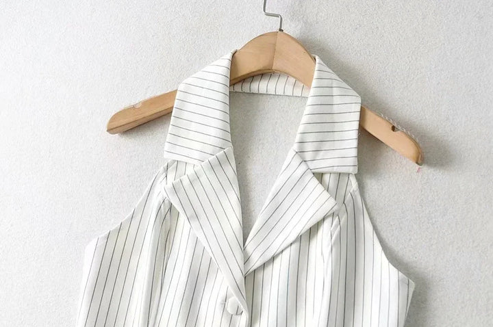 White sleeveless blouse with thin black vertical stripes on wooden hanger against white wall