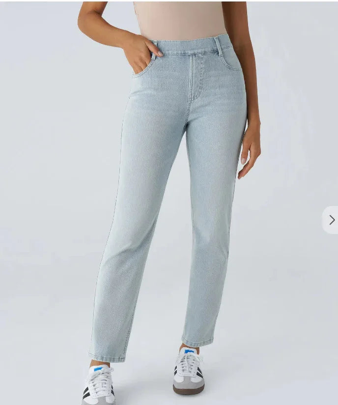 Woman wearing light wash high-waisted slim jeans and white sneakers on a plain background