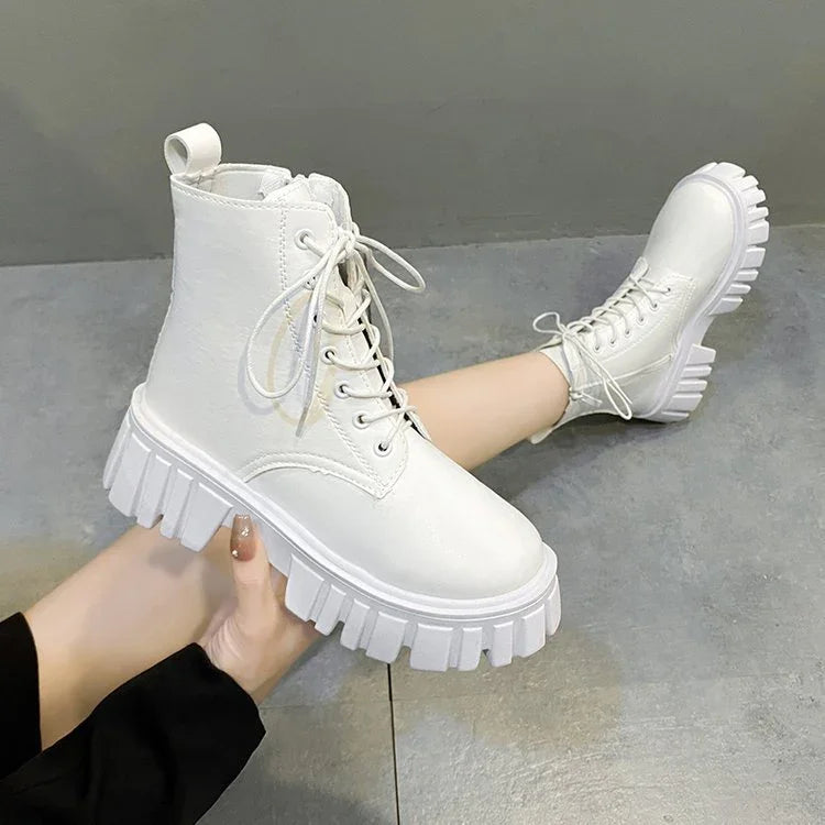 White chunky platform lace-up ankle boots worn with black pants on gray floor