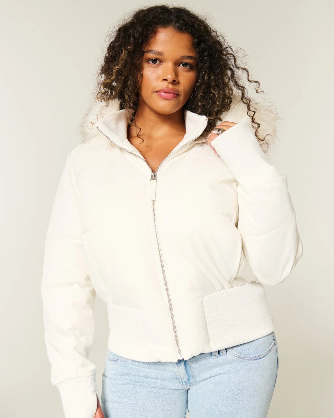 Young woman wearing a white puffer jacket with fur-trimmed hood and light blue jeans