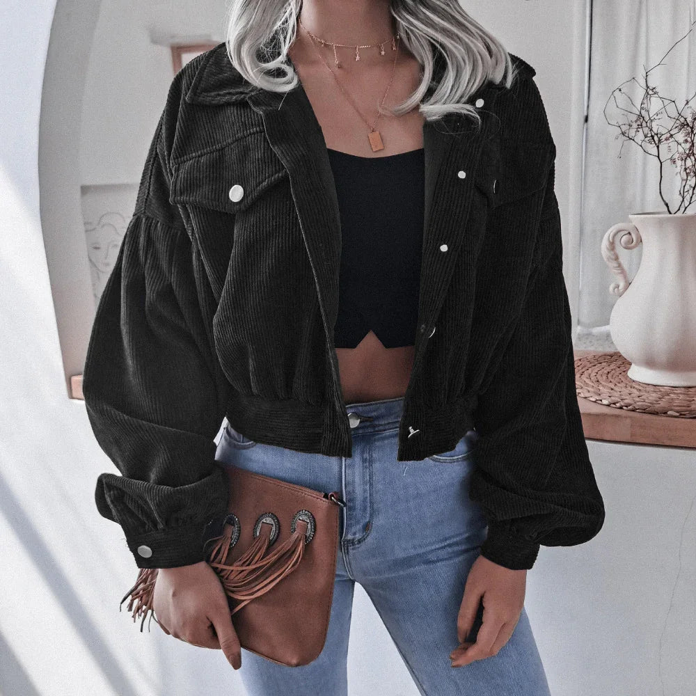 Woman wearing black cropped corduroy jacket and blue jeans holding brown fringe clutch bag indoors