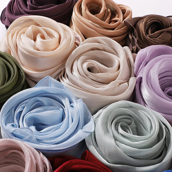 Close-up of rolled silk scarves in various colors including beige, brown, blue, green, purple, and red