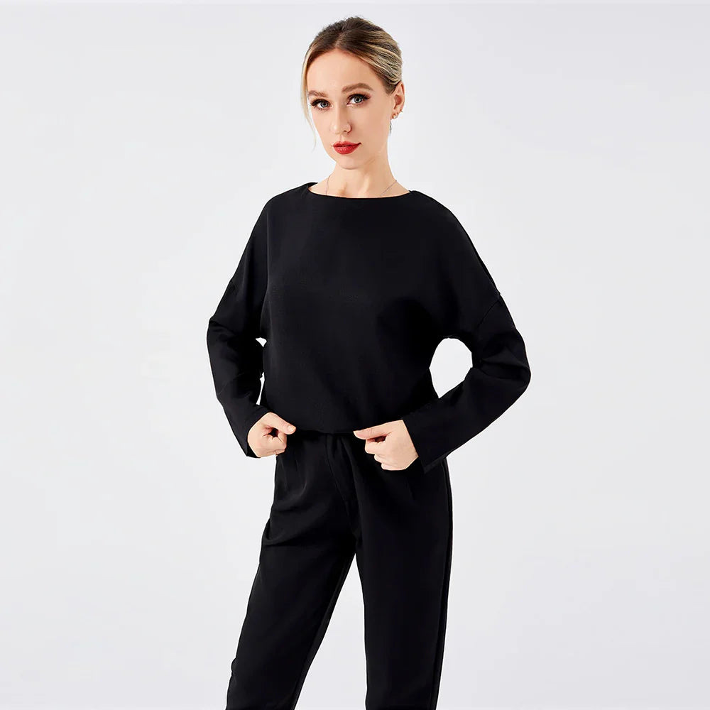 Woman wearing black long-sleeve top and pants on plain white background