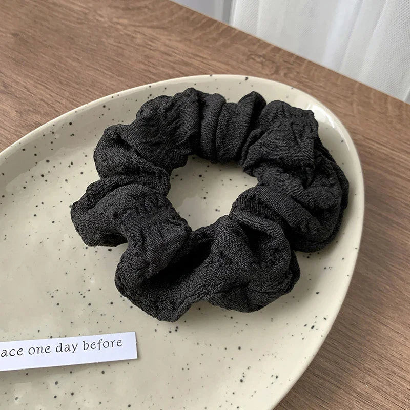 Black fabric scrunchie placed on a speckled beige ceramic plate on wooden surface