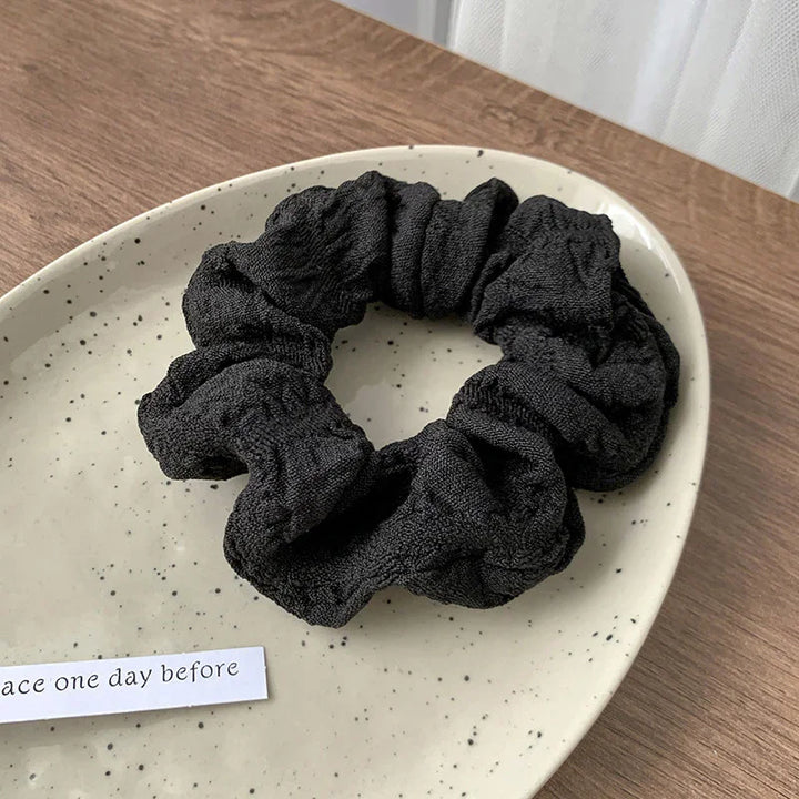 Black fabric scrunchie placed on a speckled beige ceramic plate on wooden surface