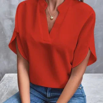 Woman wearing a vibrant red short-sleeve blouse with a split neckline and blue jeans against a gray background