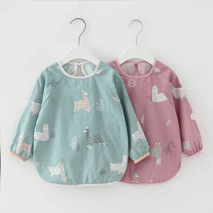 Two long-sleeve toddler bibs with llama prints, one blue and one pink, hanging on white hangers
