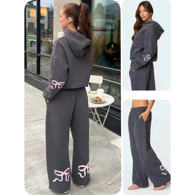 Woman wearing dark gray loungewear set with pink ribbon designs on sleeves and pant legs in outdoor cafe setting