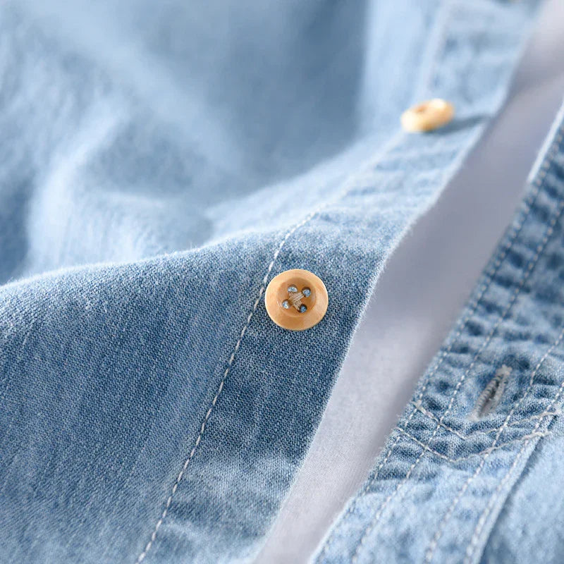 Close-up of blue denim shirt fabric with beige buttons and white stitching detail