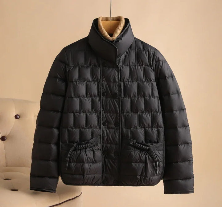 Black quilted puffer jacket with high collar and front pockets displayed on hanger against beige background