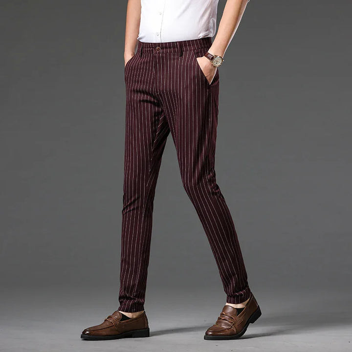 Men's burgundy slim fit pinstripe trousers paired with brown leather loafers against gray background
