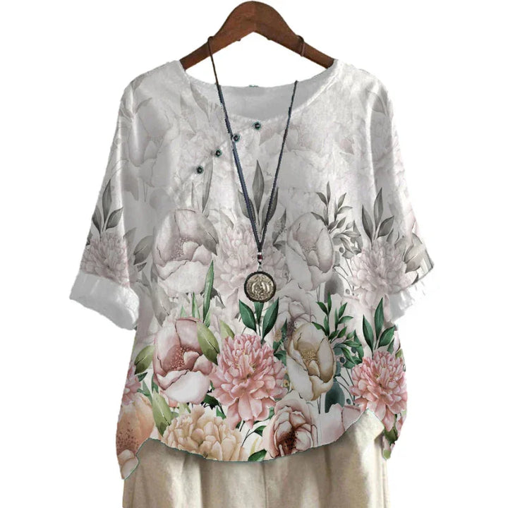 White floral print blouse with pink and green peony flowers, half sleeves, and necklace on wooden hanger
